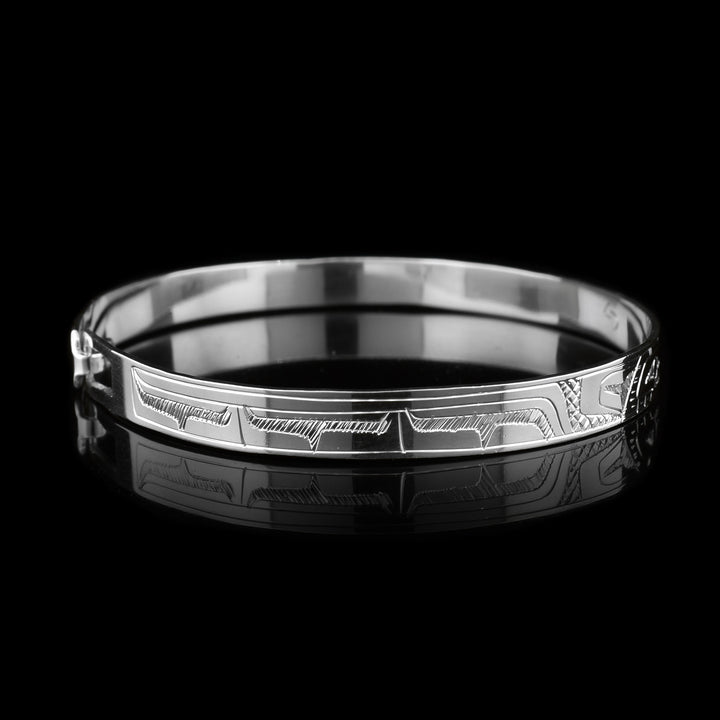 This dainty Eagle and Hummingbird bracelet has a thin, sterling silver band with a clasp in the back. There are depictions of the Eagle and the Hummingbird carved into the surface of the band. The legends are depicted facing each other. 