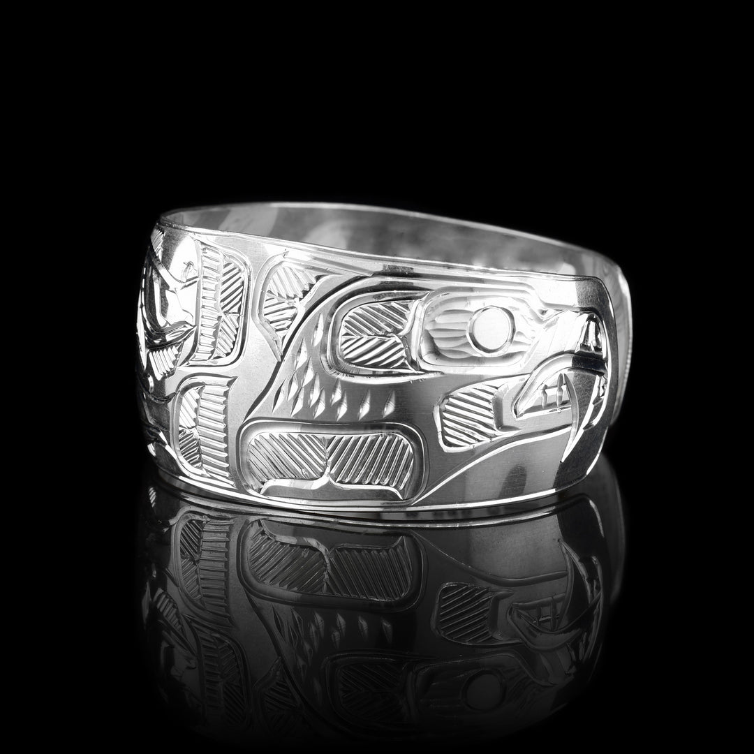 This sterling silver cuff bracelet has a wide band with depictions of the Bear and the Eagle carved onto the sides of the band and there are depictions of the Salmon carved onto the center of the band.