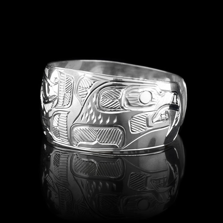This sterling silver cuff bracelet has a wide band with depictions of the Bear and the Eagle carved onto the sides of the band and there are depictions of the Salmon carved onto the center of the band.