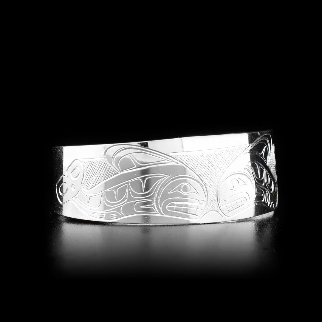 This Orca bracelet is made from sterling silver and has a wide band with a gap in the back. There are depictions of an Orca pod carved across the surface of the band.