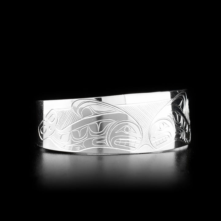 This Orca bracelet is made from sterling silver and has a wide band with a gap in the back. There are depictions of an Orca pod carved across the surface of the band.