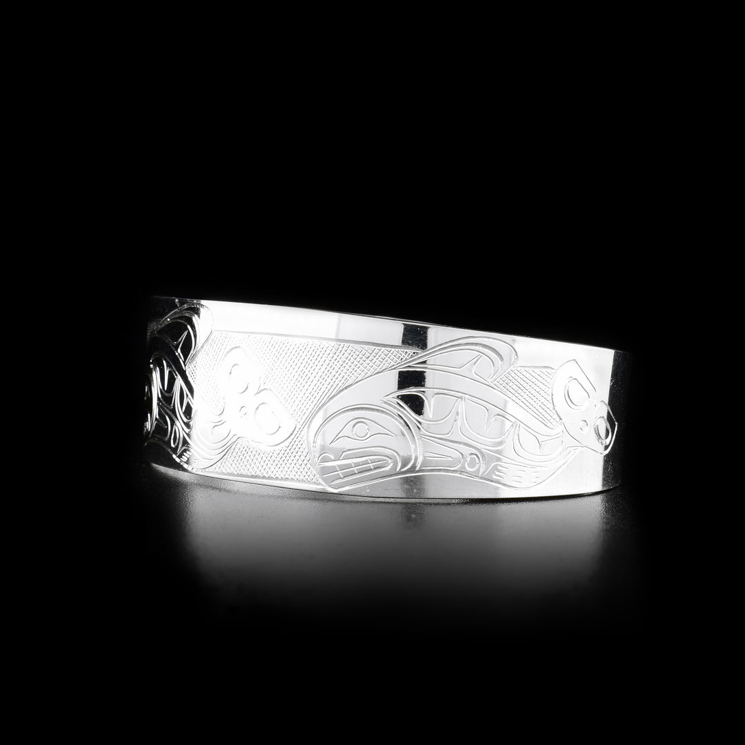 This Orca cuff bracelet is made from sterling silver and has a wide band with a gap in the back. There are depictions of an Orca pod carved across the surface of the band.