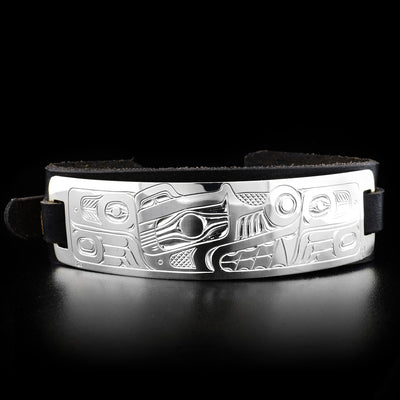 The silver plate of this bear bracelet has the head of a bear facing the right with carved details representing its paws and body on both sides. The rectangular plate is on a narrow, long piece of leather.