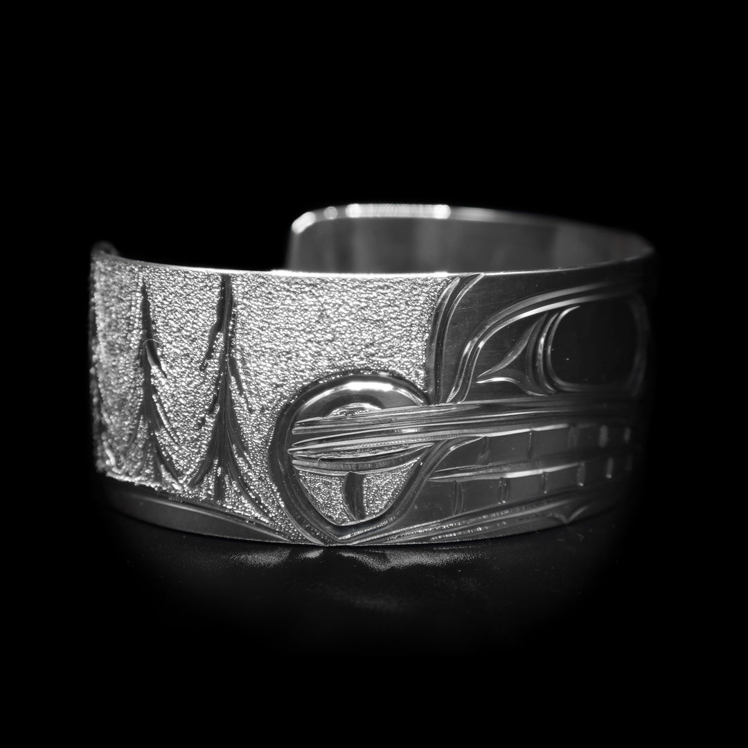 This sterling silver wide cuff bracelet has a depiction of the Beaver carved in the center of the piece and there are trees depicted in the background.