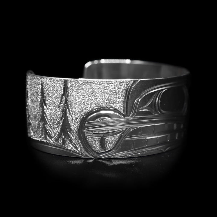 This sterling silver wide cuff bracelet has a depiction of the Beaver carved in the center of the piece and there are trees depicted in the background.
