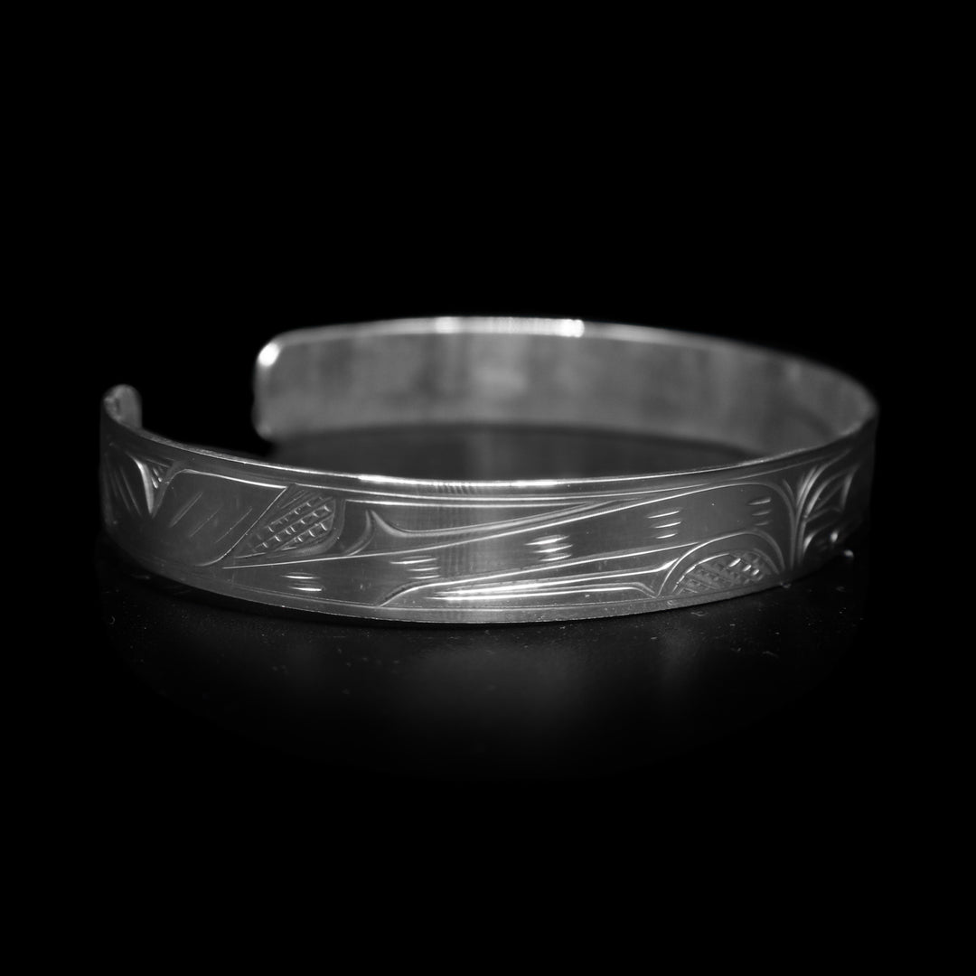 This dainty bracelet has a thin, sterling silver band with a gap in the back. The head of the Orca is carved in the center of the band and there are the backs of other whales with their dorsal fins breaching out of wave patterns. There are cross hatching patterns in the space behind the legends.