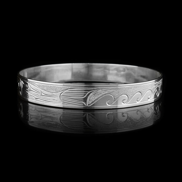 This Salmon and Orca bracelet bangle is made from sterling silver and has a single, thin band. There are depictions of the Salmon and the Orca carved across the surface of the band.
