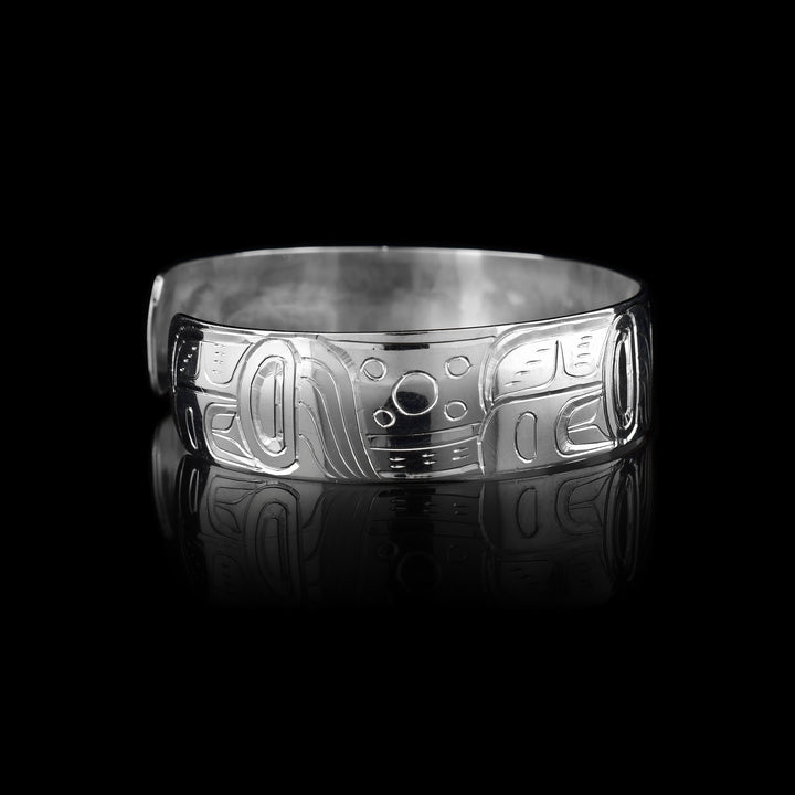 This elegant Frog bracelet cuff has a single, sterling silver band with a gap in the back. The head of the Frog is carved at a side profile in the center of the band. It is facing the right and has its tongue extending form its mouth with a spiraling curl at the end. On either side of the band the rest of the legend is depicted with its legs held at its side and having circular and triangular designs on the surface of them.