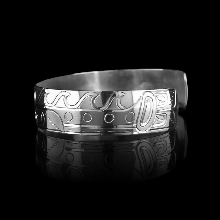 This sterling silver cuff bracelet has a single band with a depiction of the Sisiutl which is an indigenous sea serpent that has been carved into the surface of the band. The head of the serpent is in the center and around the band there is a serpent body with ridges on the top of it.