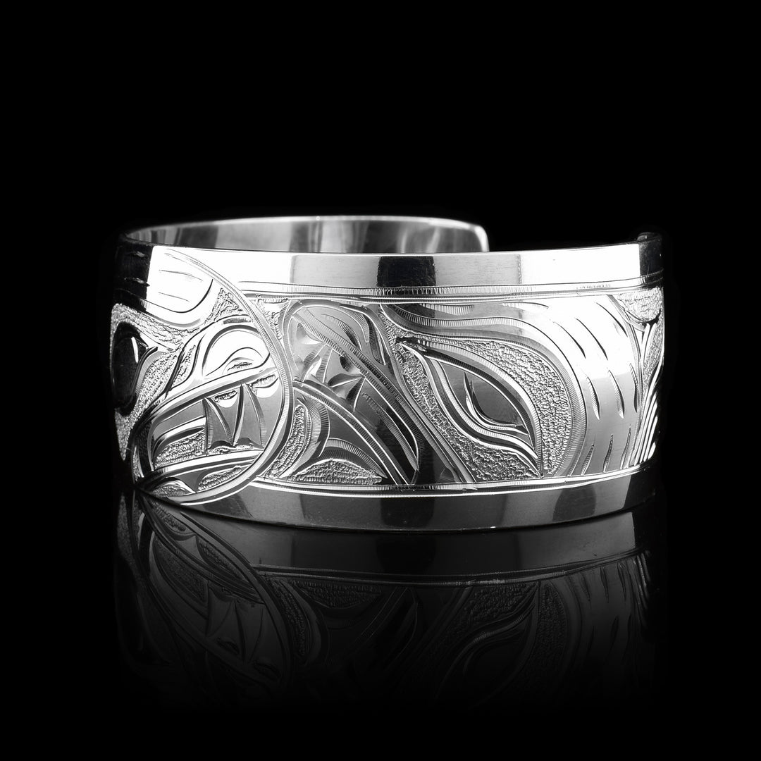 This stunning Bear bracelet is made using sterling silver and has a single, wide band with a gap in the back. There are intricate carvings on the surface of the piece that depicts the Baby Bear in the womb and being watched over by its mother who is depicted in silver and carved on the side of the piece. On the other side of the band, there are depictions the claws of the Bear.