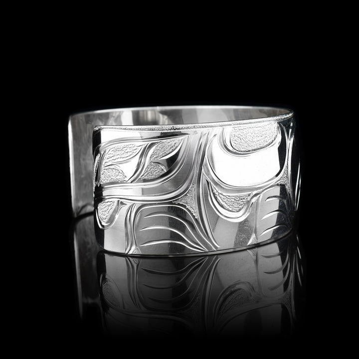 This stunning Wolf bracelet is made using sterling silver and has a single, wide band with a gap in the back. There are intricate carvings on the surface of the piece that depicts the Baby Wolf in the womb and being watched over by its mother who is depicted in silver and carved on the side of the piece. On the other side of the band, the tail of the mother Wolf is depicted..