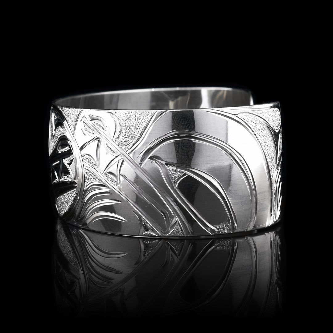 This stunning Wolf bracelet is made using sterling silver and has a single, wide band with a gap in the back. There are intricate carvings on the surface of the piece that depicts the Baby Wolf in the womb and being watched over by its mother who is depicted in silver and carved on the side of the piece. On the other side of the band, the tail of the mother Wolf is depicted..