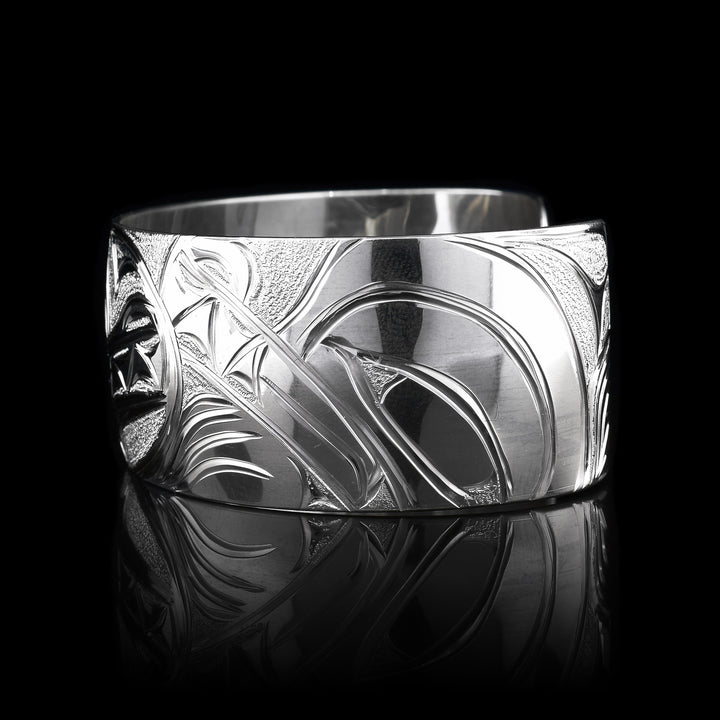 This stunning Wolf bracelet is made using sterling silver and has a single, wide band with a gap in the back. There are intricate carvings on the surface of the piece that depicts the Baby Wolf in the womb and being watched over by its mother who is depicted in silver and carved on the side of the piece. On the other side of the band, the tail of the mother Wolf is depicted..