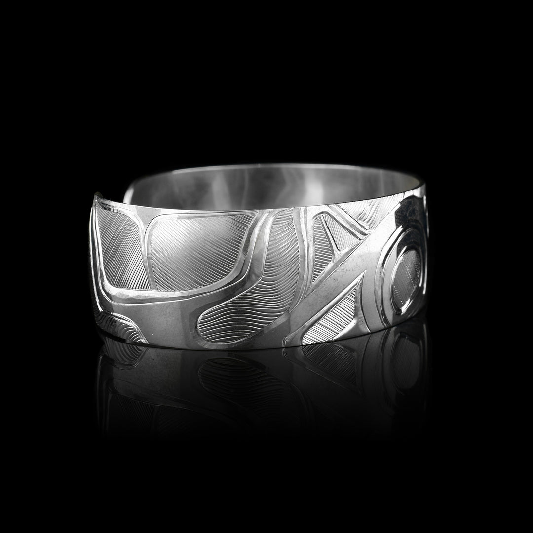 This elegant Orca bracelet cuff has a wide, sterling silver band with a gap in the back. The Orca's head and torso are carved in a side profile in the center of the band. To the left of the piece, the rest of its body is depicted. There are fine, line patterns emphasizing the details of the piece.