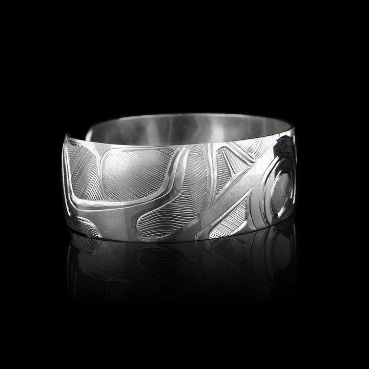 This elegant Orca bracelet cuff has a wide, sterling silver band with a gap in the back. The Orca's head and torso are carved in a side profile in the center of the band. To the left of the piece, the rest of its body is depicted. There are fine, line patterns emphasizing the details of the piece.