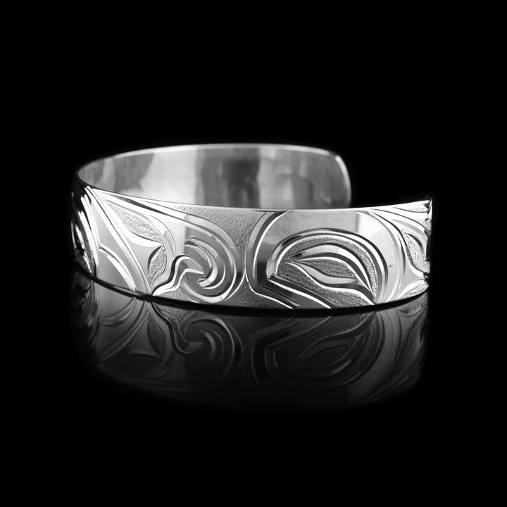 This Salmon and Thunderbird bracelet cuff has a single, sterling silver band with a gap in the back. The head of the Thunderbird is done at a side profile in the center of the band with a salmon depicted on both ends of the band.