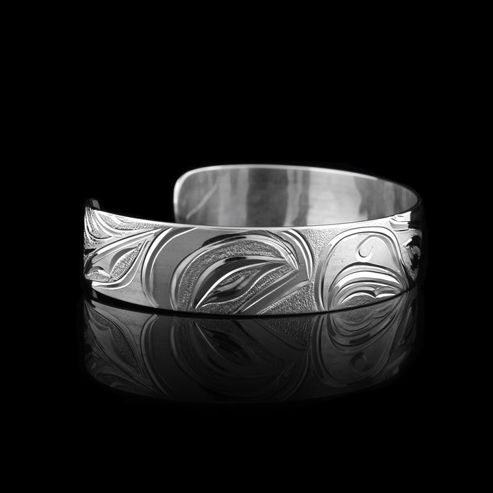 This Salmon and Thunderbird bracelet cuff has a single, sterling silver band with a gap in the back. The head of the Thunderbird is done at a side profile in the center of the band with a salmon depicted on both ends of the band.