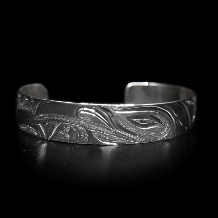 This dainty bracelet cuff has a thin, sterling silver band with a gap in the back. There is a depiction of the Raven in the night sky with the Moon legend and stars etched into the band. The head of the Raven is looking upward at the sky and extends around the majority of the band.