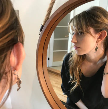 This photo shows a model looking in a mirror and wearing the earrings.