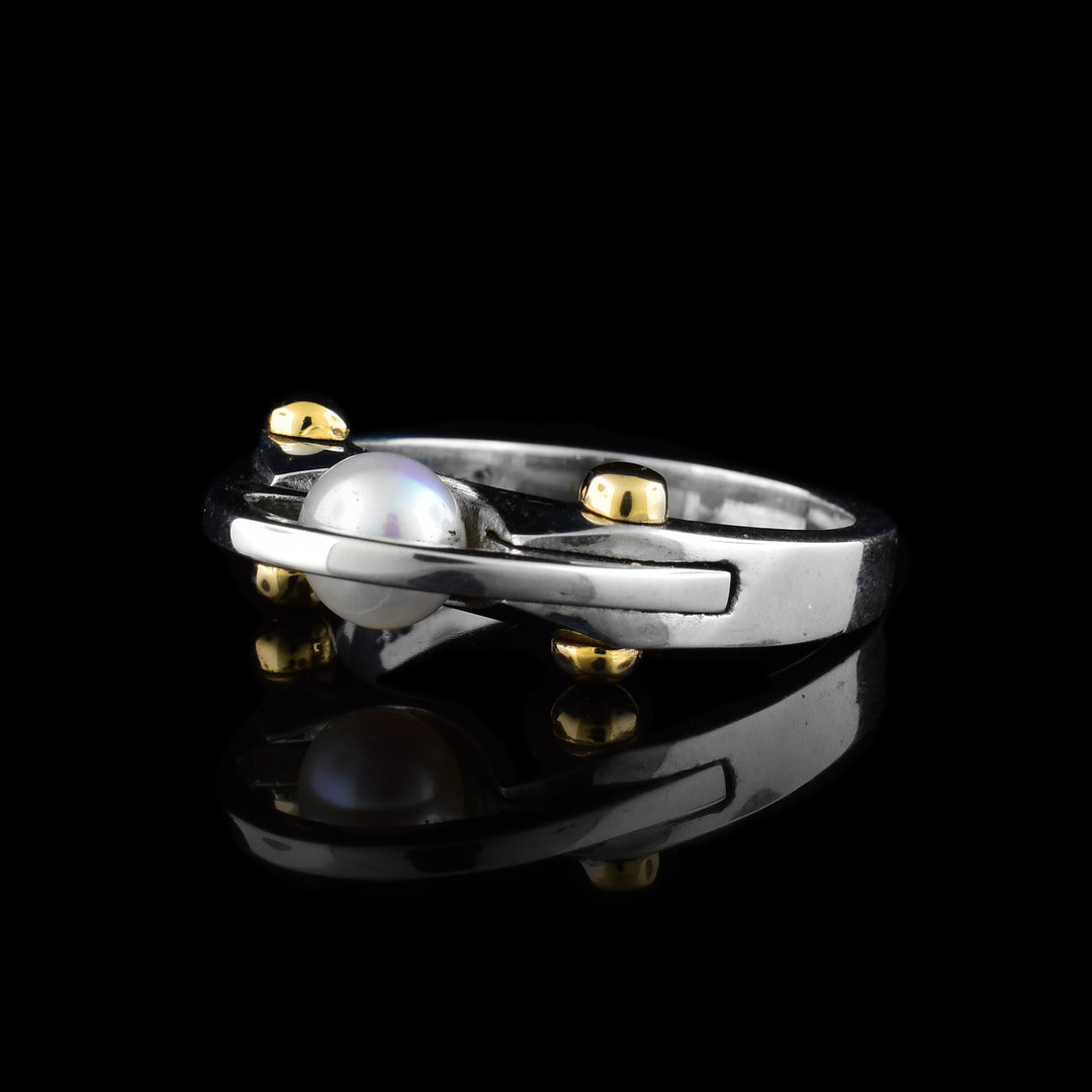 A sterling silver band with a pearl in the middle and four gold  bolt details. There is a thin silver band going over the pearl.