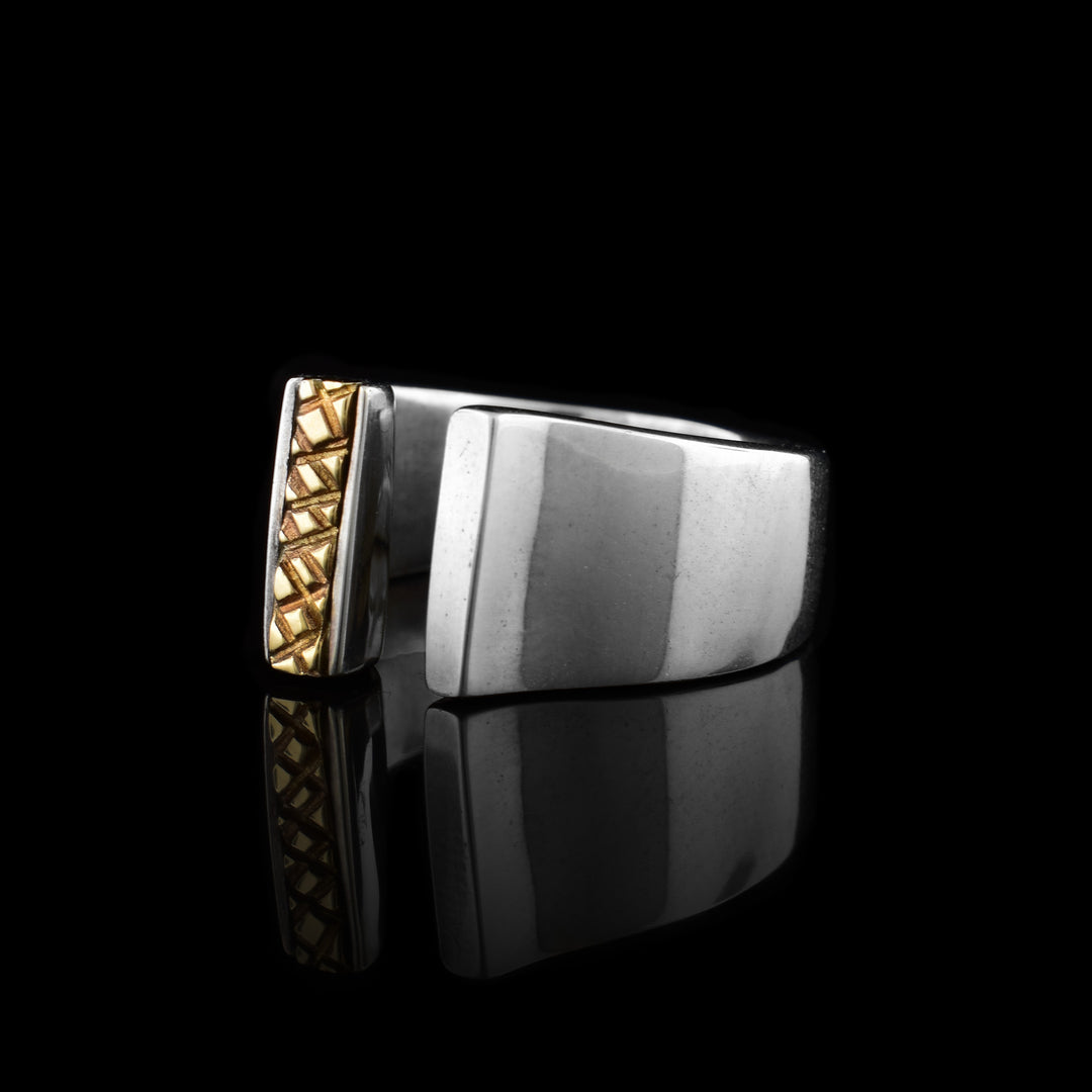 A sterling silver band that is tapered and split in the middle. One of the  sides of the band that is split has a vertical 14K gold detail on it that has a crosshatching pattern.