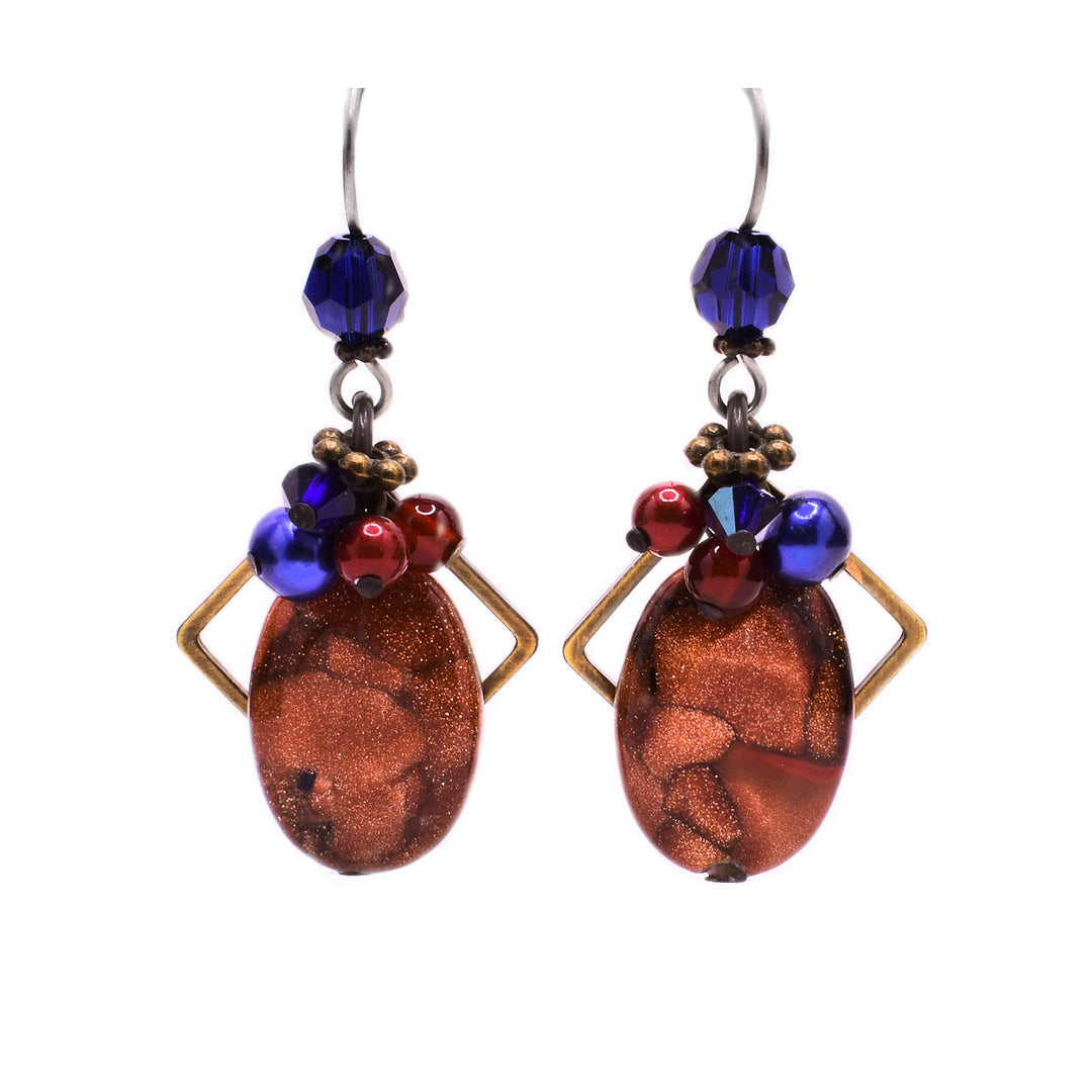 These goldstone earrings feature an oval goldstone in the center with varying gemstone accents on top and a brass diamond-shaped accent behind. At the very top is a large blue Swarovski crystal.