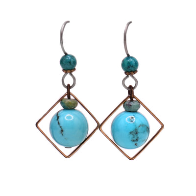 These turquoise earrings feature a turquoise ball attached to magnesite gemstones above and a diamond-shaped brass accent.