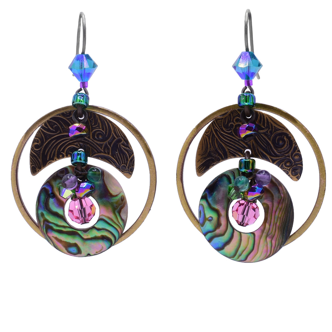 These abalone dangle hoop earrings feature a circular abalone shell with a hole in the middle as the centerpiece. In the hole is a large, pink crystal with a cluster of purple and green gemstones on top. Above is a crescent-shaped brass accent with more crystals attached. Around the entirety of the earring is a large, circular brass ring.