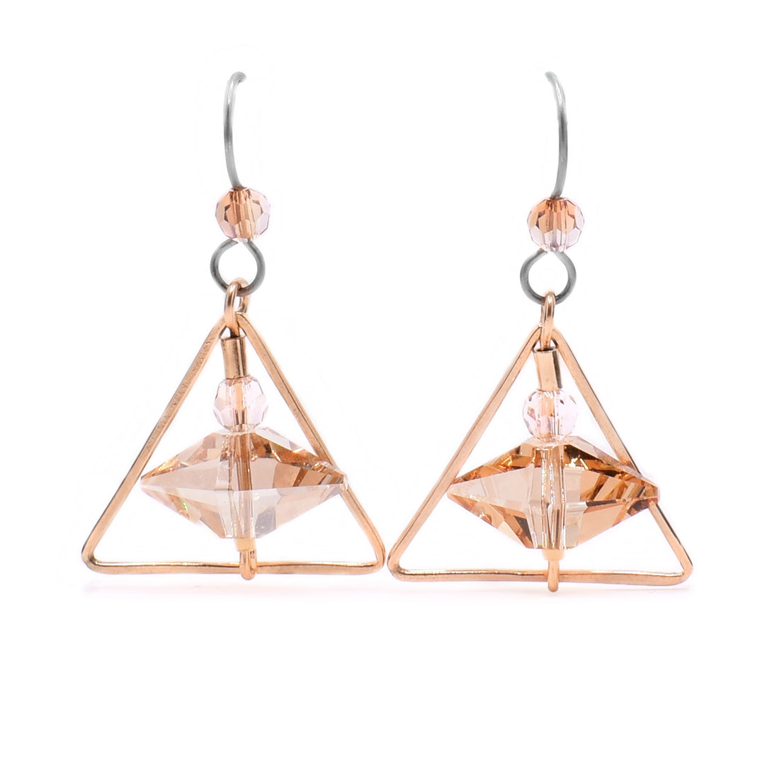 These triangle hoop earrings feature a triangular-shaped gold-filled accent with an abstract shaped crystal hanging in front of it. Above the large crystal is a smaller circular crystal bead and a gold-filled accent.