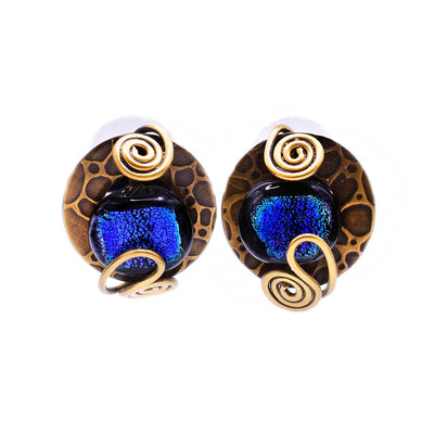 These glass stud earrings feature circular dichroic blue glass in the center and brass with a leopard print design behind it. There are squiggly brass accents on the top and bottom encasing the glass.