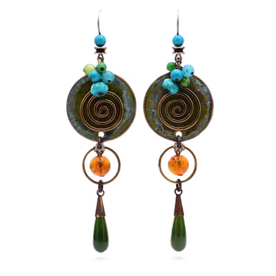 These dangle earring feature a circular aventurine piece with a squiggly brass accent and a cluster of blue and green beads at the top. Connected to it at the bottom is a circular orange Baltic Amber bead with brass accents and to that a teardrop BC jade.