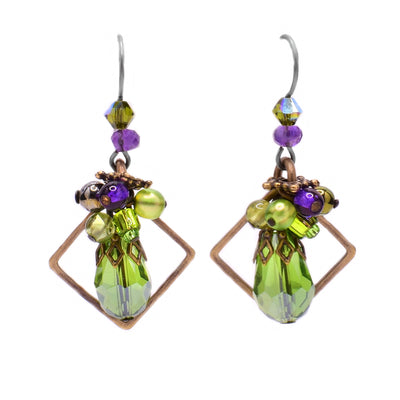 These crystal teardrop earrings feature a teardrop peridot in the center with a cluster of purple and green beads above. Behind the peridot is a diamond-shaped brass accent. Attached to the hook is an amethyst bead and a green glass bead.