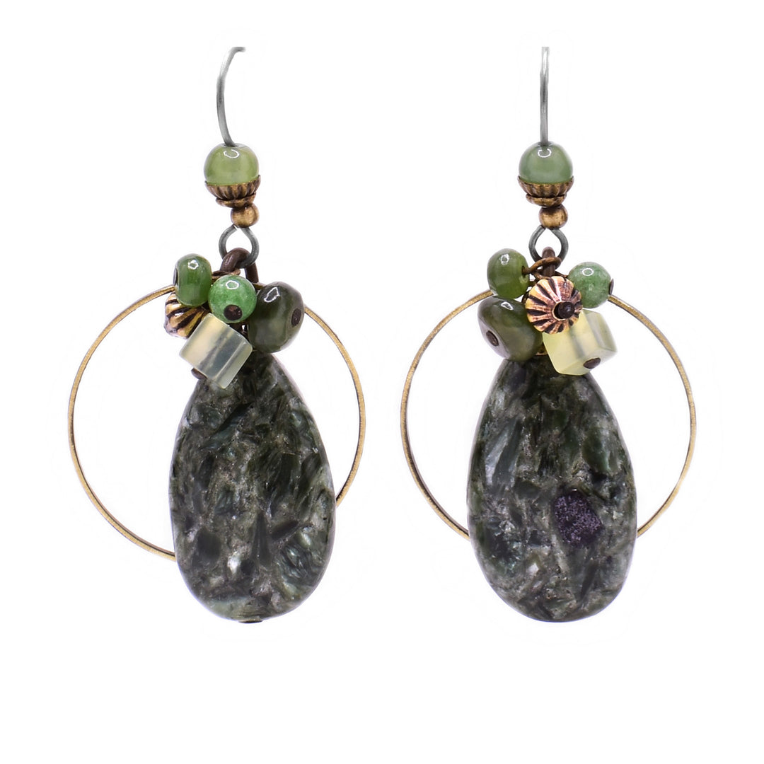 These teardrop funky earrings feature an oval seraphanite gemstone centerpiece with a large, thin brass accent behind it. On top the seraphanite is a cluster of green beads and above the cluster is a light green jade bead.