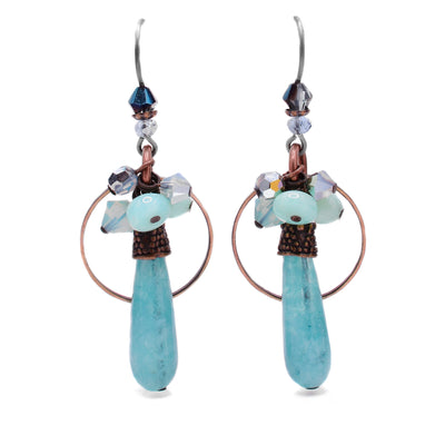 These raindrop earrings feature a teardrop-shaped light blue quartz as the centerpiece with a circular, thin brass accent behind. Above the blue quartz is a cluster of various light blue gemstones and glass beads. At the very top under the hook is a dark blue Austrian crystal.