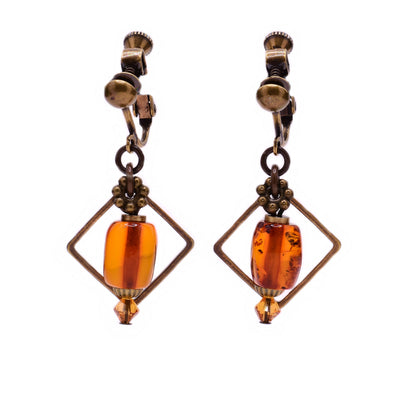 These amber earrings feature a large amber piece in the center with a diamond-shaped brass accent behind and a small, orange Austrian crystal attached at the bottom.