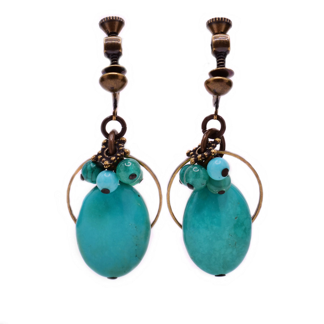 These clip earrings feature an oval turquoise as the centerpiece with a cluster of light blue and green gemstones above. There is a thin, circular brass accent behind the turquoise and additional brass accents on top of the cluster.
