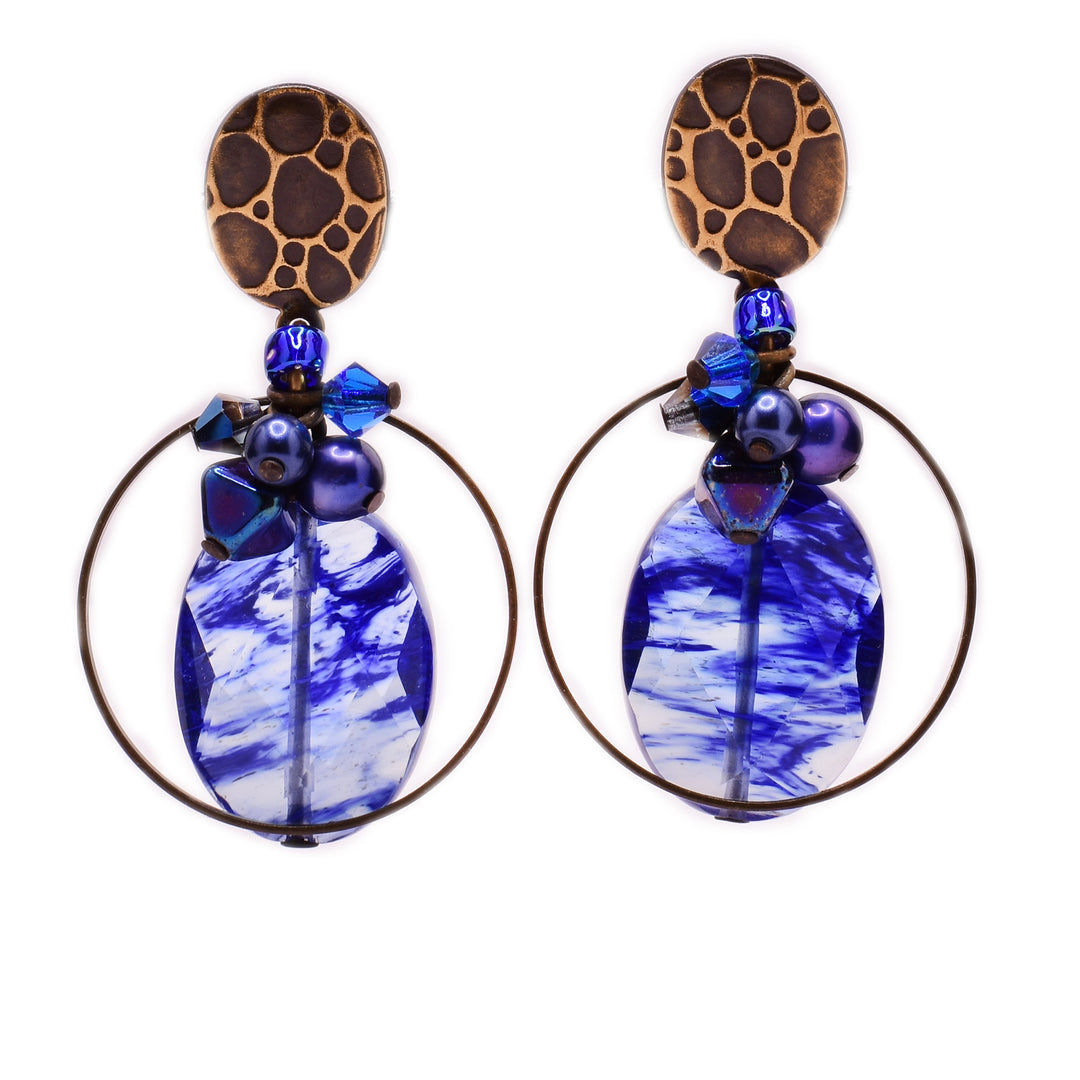 These glass stud earrings feature an oval, blue glass in the center with a cluster of dark blue and purple beads on top and a very thin, brass circle around the glass. The post is brass and has a leopard print on it.