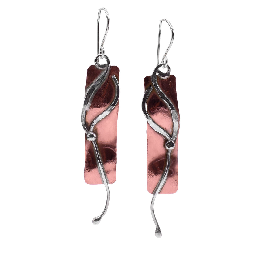 These dangling ocean earrings have long, rectangle shaped hangs made from copper. These hangs have been slightly bent into a wavy shape. There are thin pieces of sterling silver paced on the hangs depicting pieces of bull kelp (sea kelp). The sterling silver extends past the copper hangs at the bottom.