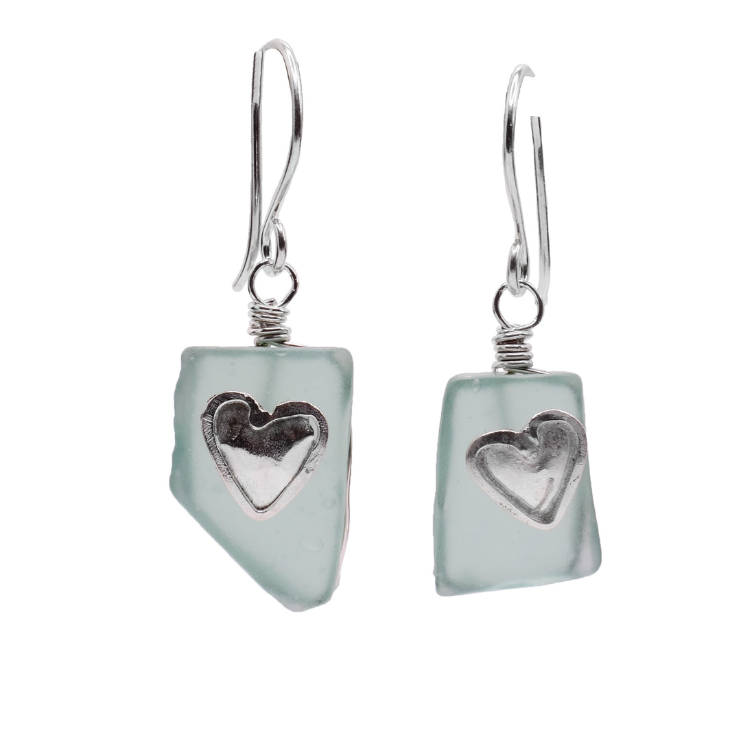 These glass heart earrings have rough, rectangle shaped hangs made from turquoise sea glass. There are heart shaped charms made from sterling silver that are placed on the glass hangs.