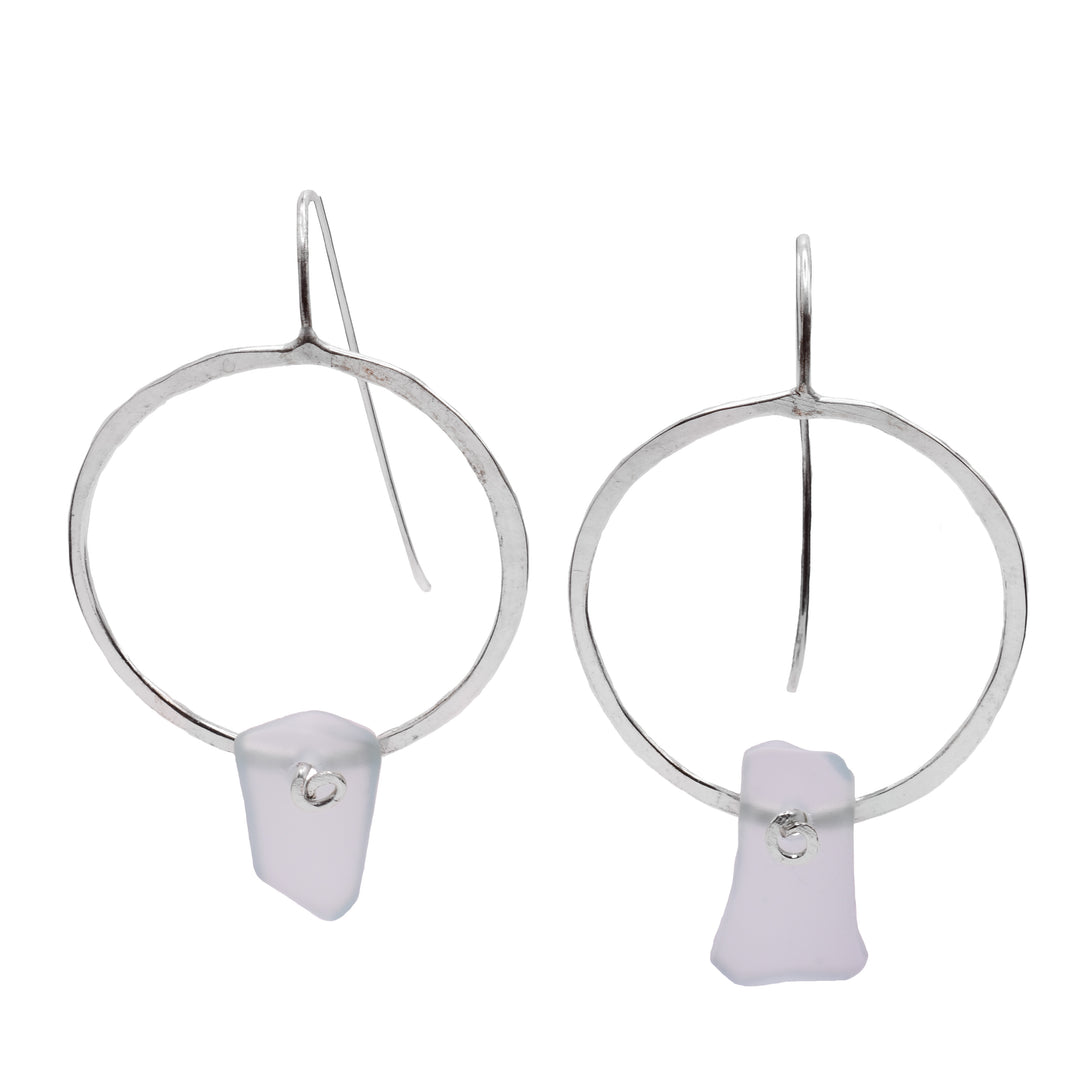 These sea glass silver earrings hoops have sterling silver hoops that are flat and roughly shaped. There are longer, clear pieces of sea glass attached to the bottom on the hoops.