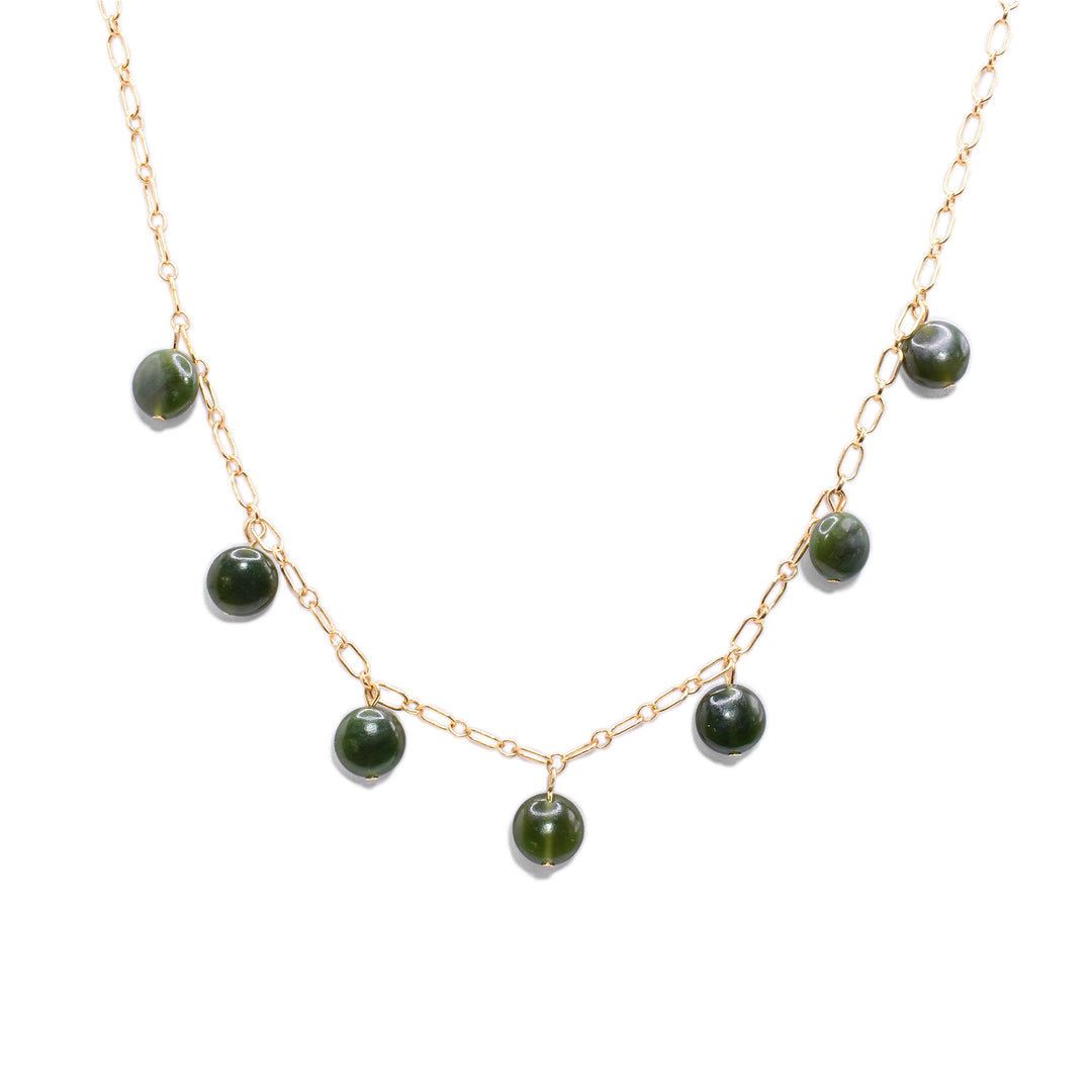 This jade charm necklace has a simple 14K gold filled chain with 7 jade beads at the bottom half of the piece. The jade charms are small, circular and flat.