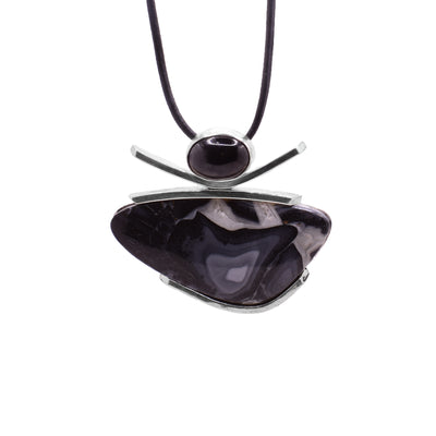 This maligano jasper necklace features an assymetrical oval-shaped jasper with linear silver accents above and an oval black spinel gemstone resting on top. The leather cord is attached at the back of the spinel gemstone.
