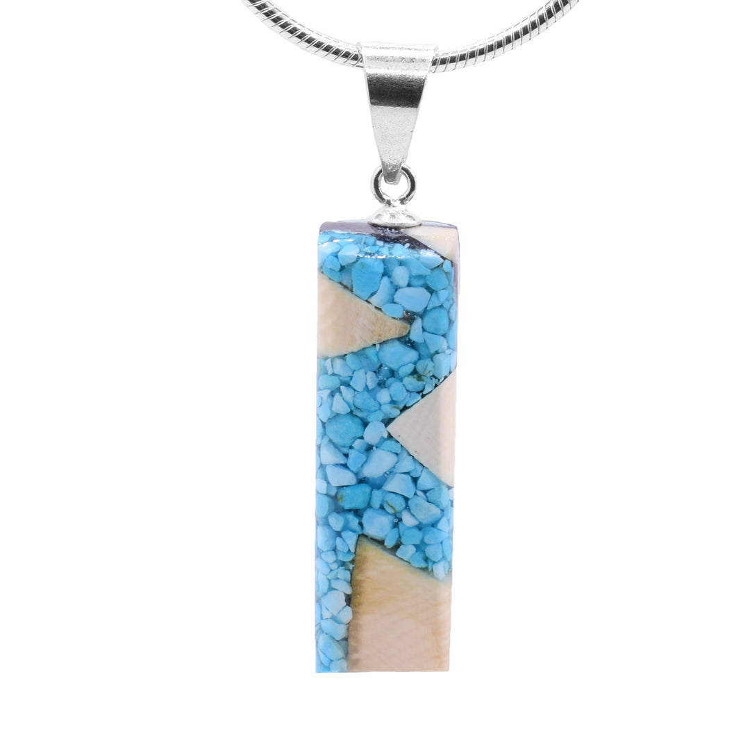 This turquoise pendant is made from fossilized mammoth ivory and turquoise gemstones. Pieces of turquoise and chunks of ivory have been set in resin and shaped into a thin rectangle.