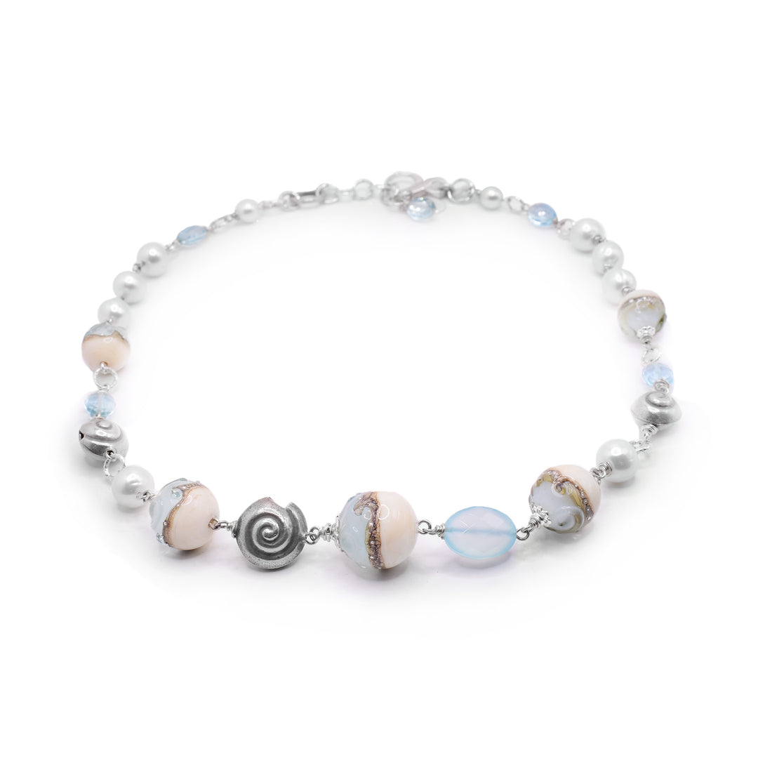 This pearl charm necklace is made up of beads made from various materials and shapes. There are larger, sphere shaped beads with blue and pink glass and a wave pattern going through the center of them. These rest of the piece is made from pearls and tumble, turquoise glass beads with shell, shaped sterling silver charms.