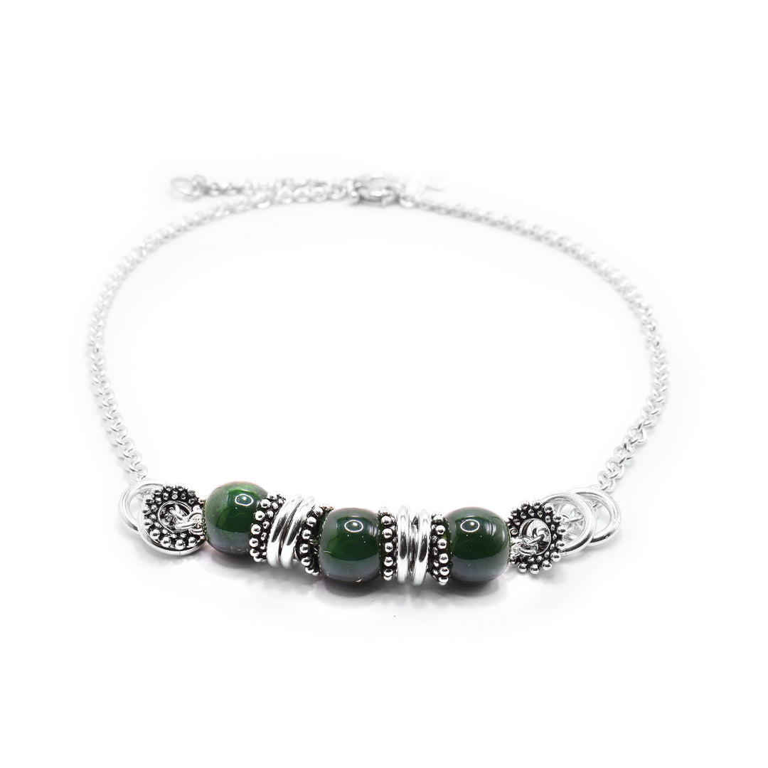 This jade charm necklace has a dainty chain with jade beads and sterling silver charms at the bottom portion of the piece. There are three jade beads separated by thin, silver charms that are made of small spheres.