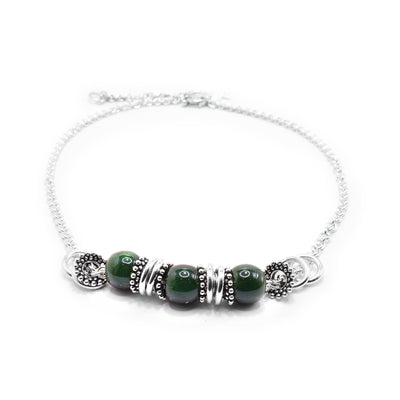 This jade charm necklace has a dainty chain with jade beads and sterling silver charms at the bottom portion of the piece. There are three jade beads separated by thin, silver charms that are made of small spheres.