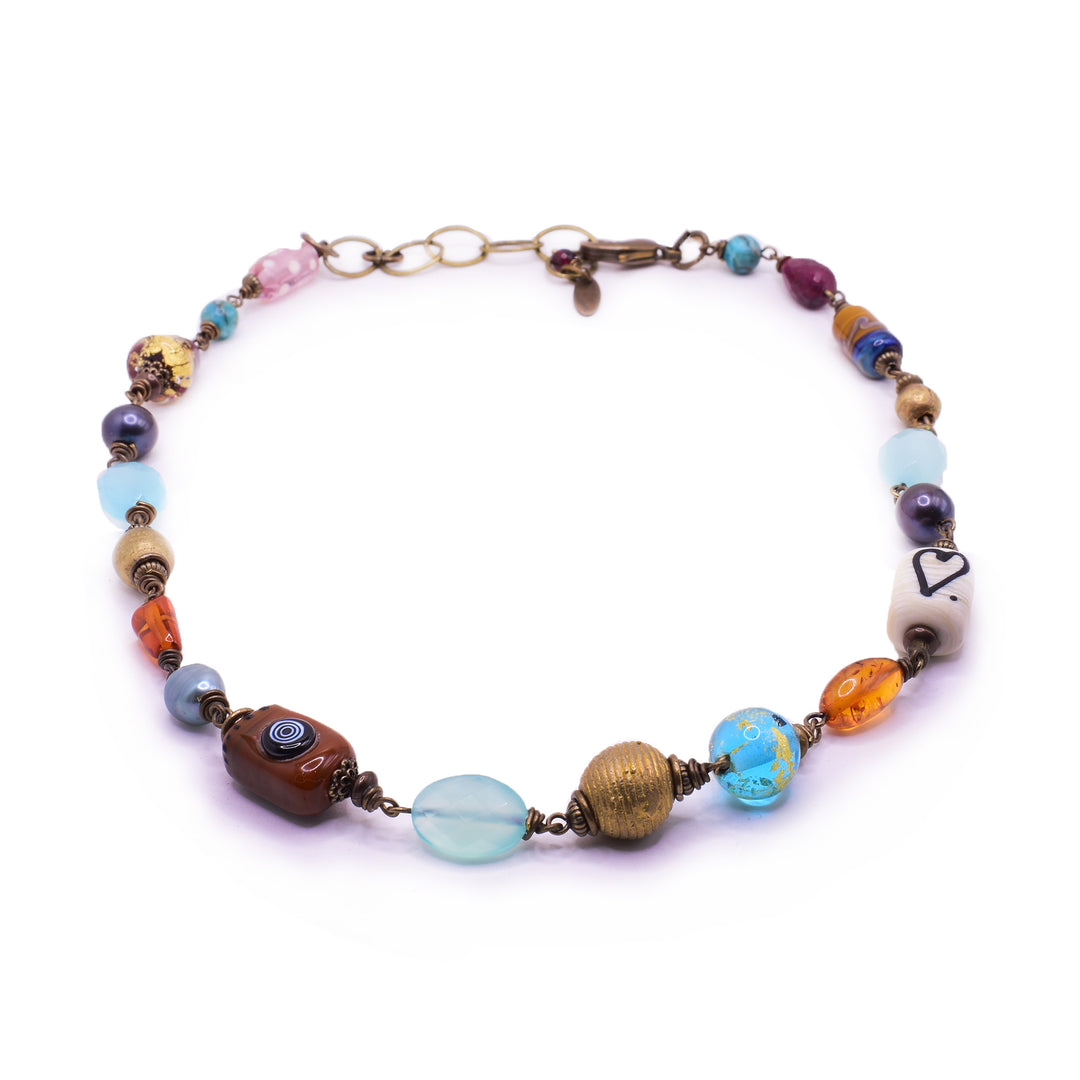 This bead charm necklace is made from an assortment of glass bead that all have different sizes, shapes and colors. there are two larger rectangle beads, one is white with a heart and the other is red with a blue, spiral design on it. On the sides of the piece, there are sphere shaped beads made from a brilliant aquamarine gemstone. The piece is held together using braass.