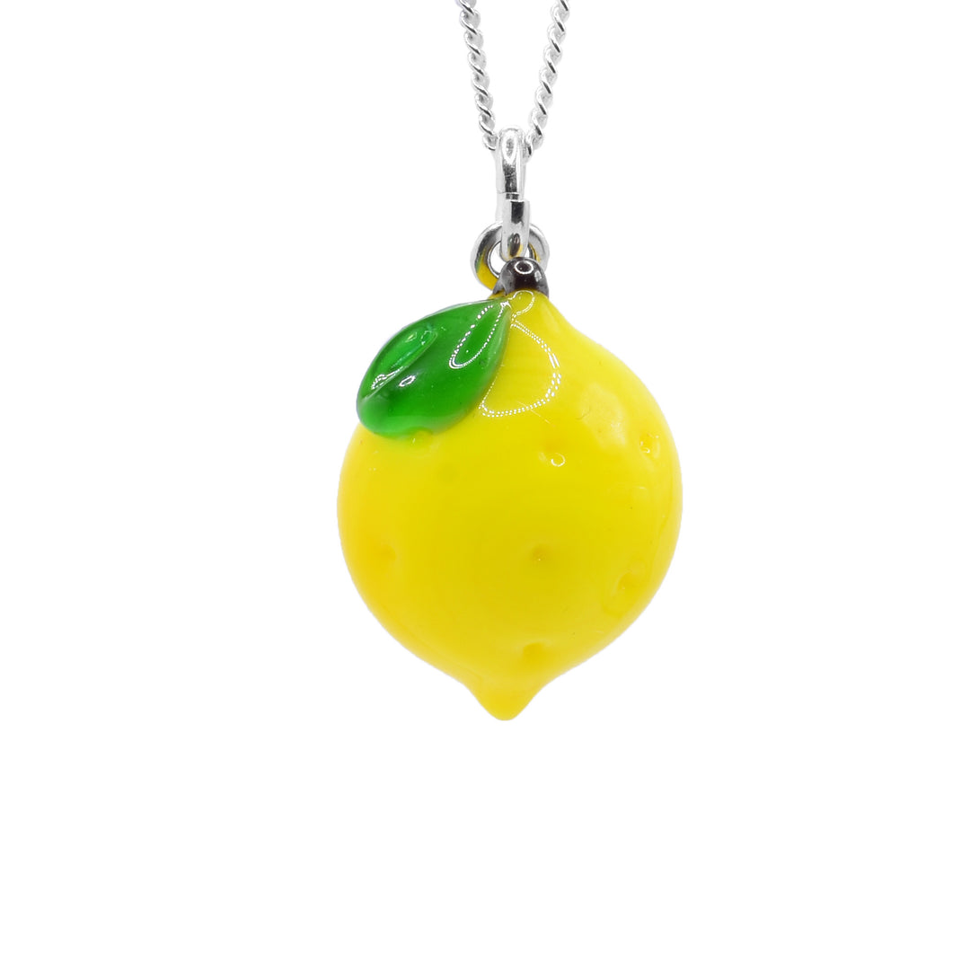 This Lemon necklace has a lampworked glass charm that is a Lemon. The pendant has yellow glass that is oblong and lemon shaped with dimples made in the surface of it. There is a single, green leaf at the top of the piece.