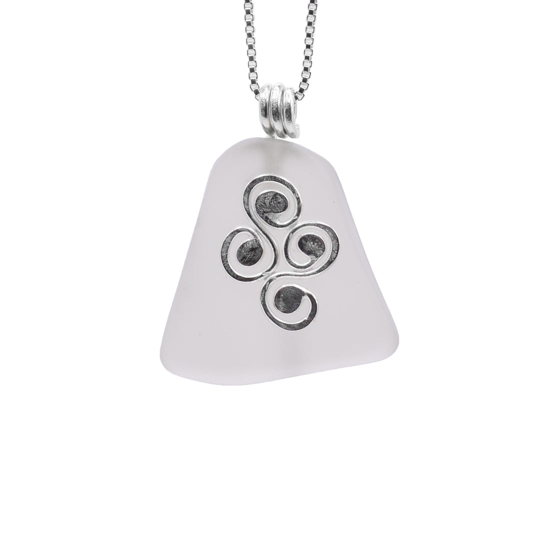 This sea glass pendant has a trapezoid shaped piece of White Sea glass. In front of the glass, there is a sterling silver charm with four swirling designs resembling water.