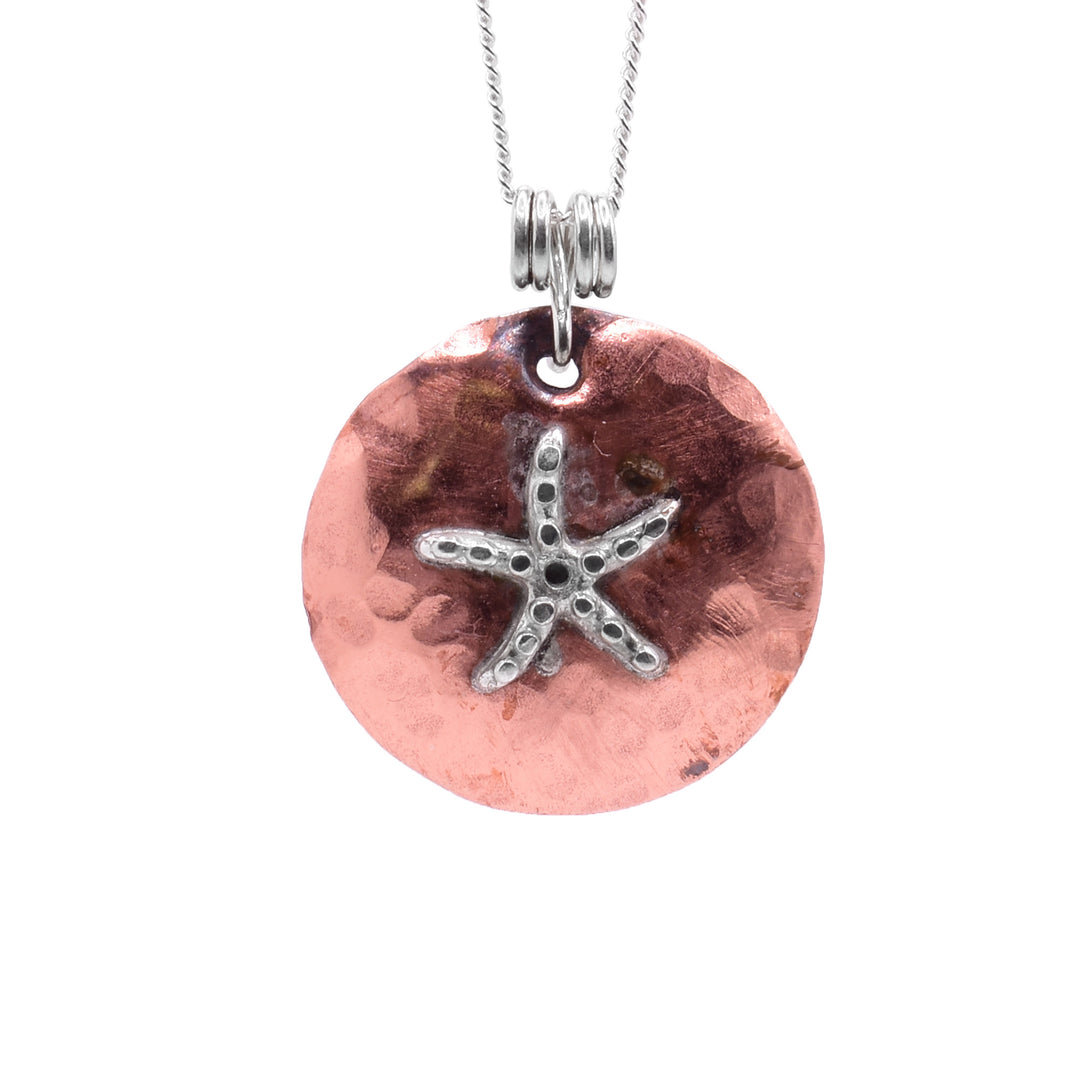 This starfish pendant has a circle shape made from copper and a sterling silver starfish in the center of it. There are circle dots made in the surface of the starfish charm.